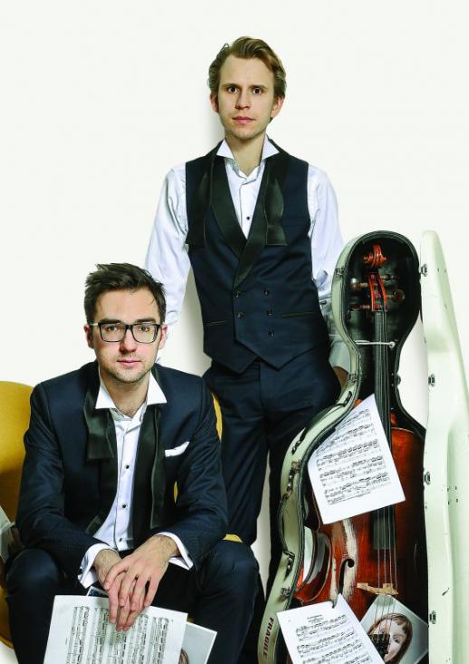 a young seated man and a young man standing next to a cello in an open case