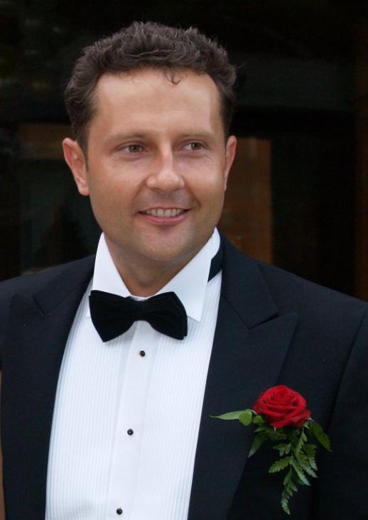 A man in a white shirt and black jacket, with a rose in his buttonhole