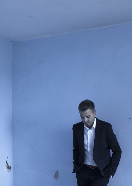 mężczyzna w garniturze opierający się o zniszczoną, błękitną ścianę