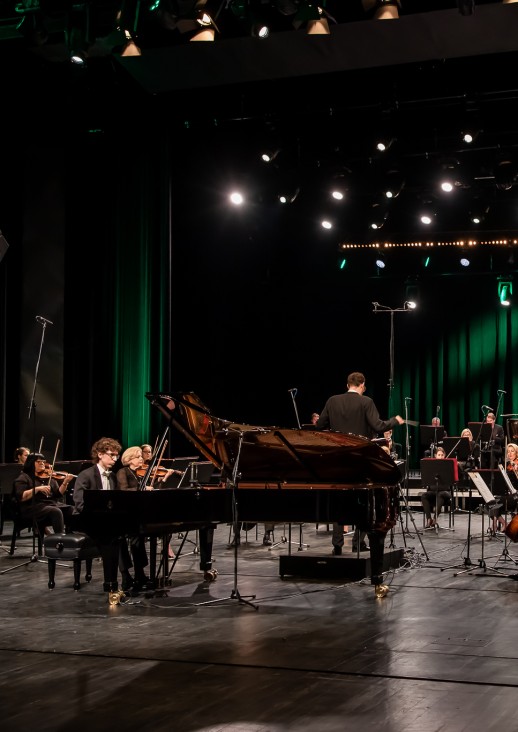 pianista siedzi przy fortepianie i orkiestra siedząca na scenie