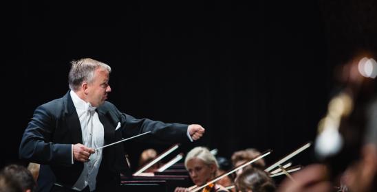 conductor holding the baton in one hand with the other hand extended