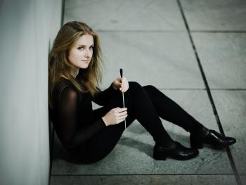 młoda kobieta, blondynka siedząca, oparta o ścianę, w ręce trzyma batutę