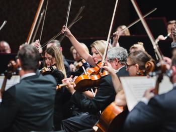 muzycy Toruńskiej Orkiestry Symfonicznej na scenie z uniesionymi smyczkami 