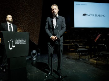 Mężczyzna przemawiający do mikrofonu na scenie, w tle logotyp Nova Trading SA