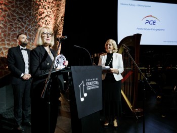 Kobieta przemawiająca do mikrofonu na scenie, w tle logotyp firmy Polska Grupa Energetyczna 
