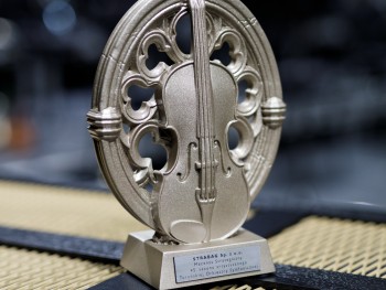  statuetek w kształcie skrzypiec wkomponowanych w okrągłe gotyckie rozety, u dołu tabliczka z zapisem Mecenas Strategiczny 45 sezonu Toruńskiej Orkiestry Symfonicznej