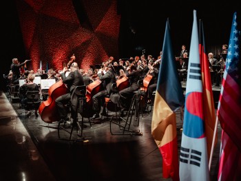 orkiestra na scenie, na pierwszym kadrze flagi różnych Państw